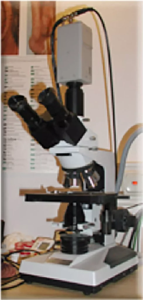 Dunkelfeldmikroskop auf einem Tisch in einer Praxis mit medizinischen Postern im Hintergrund zur Diagnostik bei