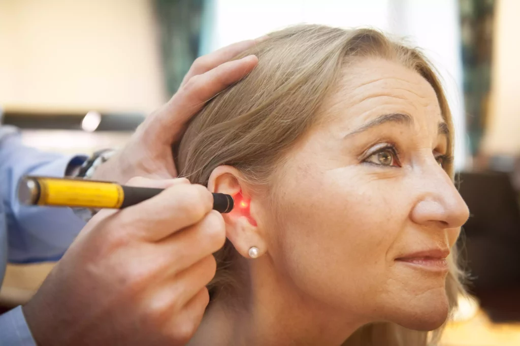 Frau erhält sanfte Laser-Therapie am Ohr zur Behandlung in einer naturheilkundlichen Praxis gegen Rückenschmerzen.