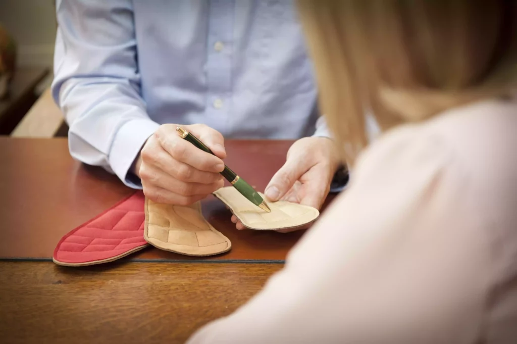 Chiropraktiker zeigt mit Stift auf verschiedene sensomotorische Einlagen während Beratung am Holztisch