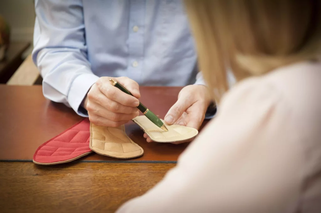 Beratungsgespräch mit Fokus auf zwei Einlagenmuster auf einem Holztisch, Person zeigt mit Stift auf eine Einlage