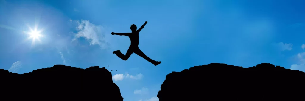 Silhouette einer Person, die bei sonnigem Himmel von einem Felsen zum anderen über eine Schlucht springt, Berglandschaft.