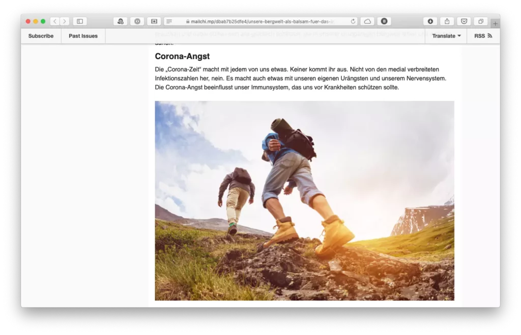 Zwei Wanderer mit Rucksäcken steigen bei Sonnenschein einen felsigen Bergpfad hinauf, umgeben von grüner Wiese und Bergen.