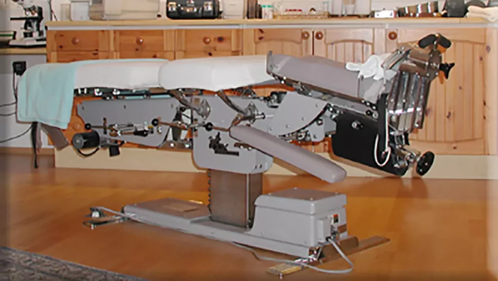 Chiropraktik-Therapietisch Cox-Tisch mit verstellbaren Polstern in Praxisraum mit Holzmöbeln und Holzboden