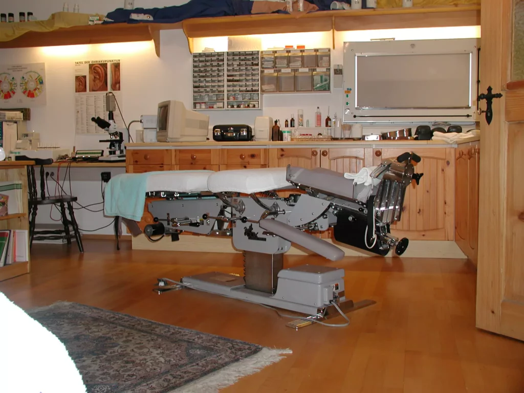 Behandlungsraum mit elektrischem Cox-Tisch für sanfte Chiropraktik, Holzschränken und medizinischen Geräten im Hintergrund