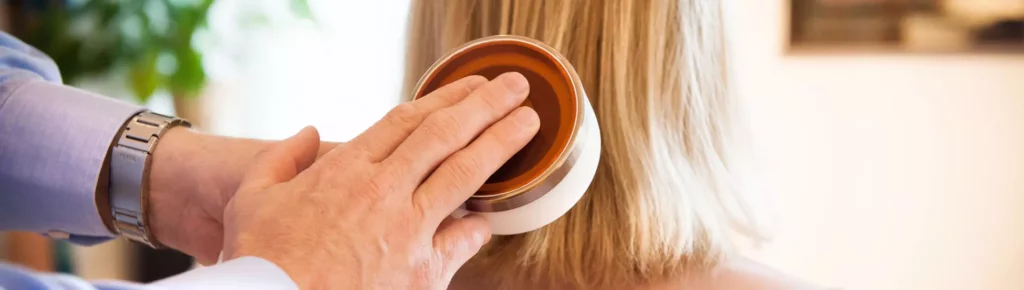 Hand eines Chiropraktikers mit Metallarmband berührt sanft den Nacken einer Frau mit blonden Haaren bei Behandlung