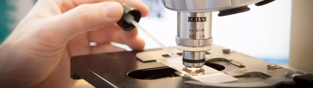 Hand tropft Flüssigkeit auf Objektträger unter Zeiss-Mikroskop in Praxis für Naturheilverfahren in Bayern