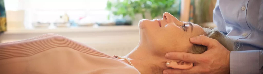 Frau liegt entspannt auf Behandlungsliege, Chiropraktiker hält sanft ihren Kopf zur Wirbelsäulenbehandlung in Bayern
