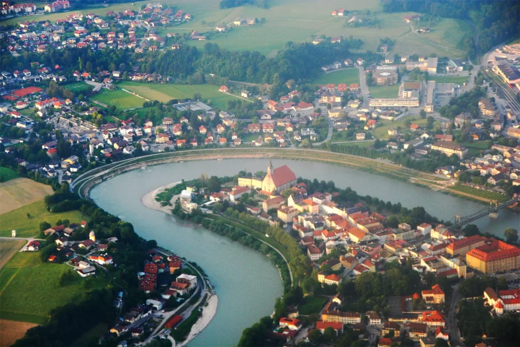 Luftaufnahme der Stadt Laufen mit Fluss, Brücke und markanter Kirche im Zentrum, umgeben von Wohngebieten und Grünflächen
