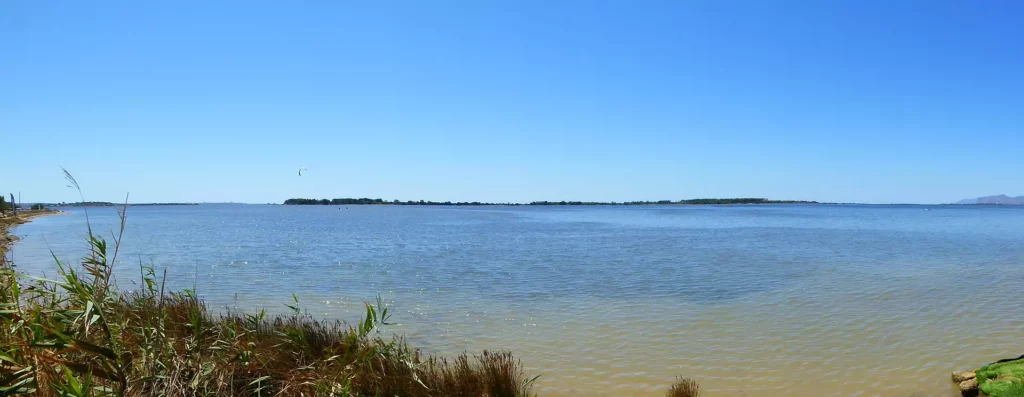 Küstenlandschaft mit ruhigem Wasser, blauem Himmel und einem Kitesurfer in der Ferne bei klarem Wetter